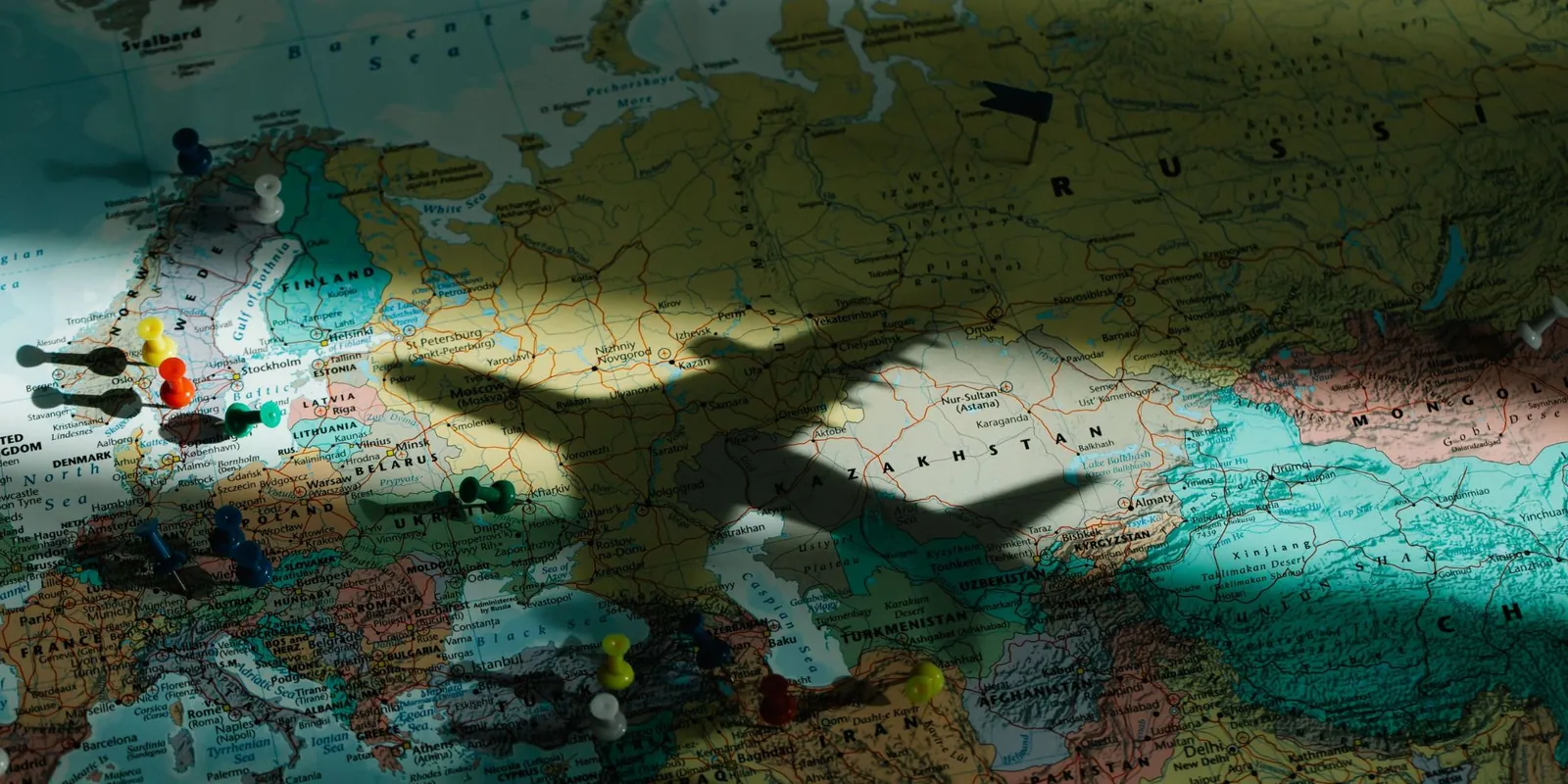 The shadow of a toy plane cast over a paper map of Europe and Asia dotted with pins.